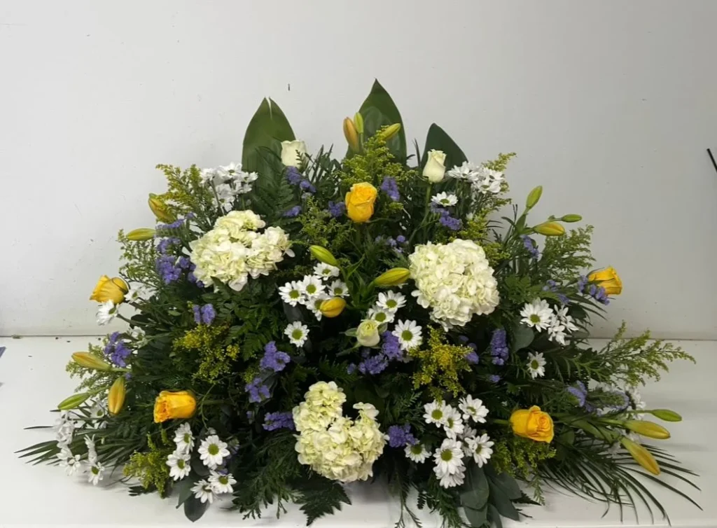 Centro floral funerario compuesto por margaritas, rosas amarillas y hortensias, un arreglo delicado y elegante para momentos de despedida